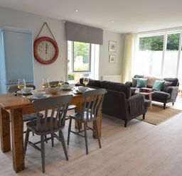 A dining area with wooden table and chairs and a living room with sofas and a coffee table at Sweet Pea Southwold