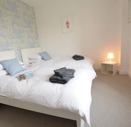 A bedroom with two single beds, white bedding, blue pillows, folded dark towels, a small white bedside table with a lamp and books, and blue wallpaper at Sweet Pea, Southwold