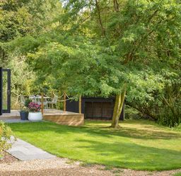 A garden with a tree and a wooden deck with outdoor furniture at Spexhall Barns in Halesworth