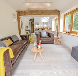 A living room with brown leather sofas, a wooden beam, and large windows at Spexhall Barns in Halesworth