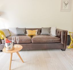 A brown leather sofa with cushions and a yellow throw next to a wooden side table with a bottle in an ice bucket and two glasses at Spexhall Barns in Halesworth
