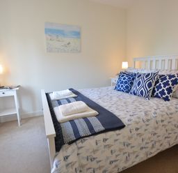 A bedroom with a bed with white and blue bedding and pillows two bedside tables with lamps and a painting on the wall at Mycroft Southwold in Southwold