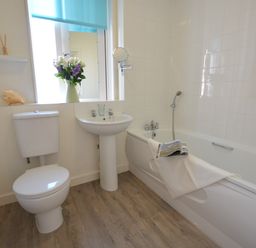 A bathroom with a toilet sink bathtub flowers on the window sill at Mycroft Southwold in Southwold