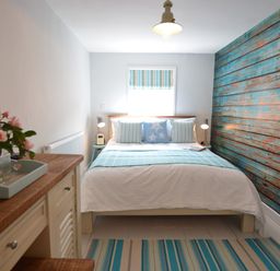 A bedroom with a bed against a blue wooden paneled wall and a wooden dresser with flowers on it at Alinka Aldeburgh in Aldeburgh