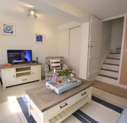 A living room with a coffee table holding a tray with flowers and drinks a patterned armchair a television on a cabinet a floor lamp and stairs at Alinka Aldeburgh in Aldeburgh