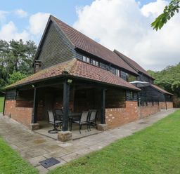 An outdoor patio area with a table and chairs next to a brick and wood house surrounded by grass and trees at Quill Farm Barn in Campsea Ashe