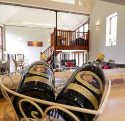A living area with two bottles of prosecco in a basket on a wooden counter and wooden furniture at Quill Farm Barn in Campsea Ashe