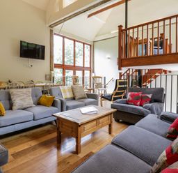 A living room with grey sofas a wooden coffee table dining table with chairs and wooden railings at Quill Farm Barn in Campsea Ashe