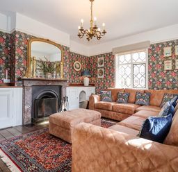 A living room with a large L shaped brown sofa and ottoman by a fireplace and a patterned rug at Church Farm Dunwich Near Westleton