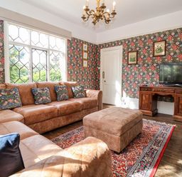 A living room with a brown leather sofa and ottoman a patterned rug a wooden TV stand with a television and floral wallpaper at Church Farm Dunwich Near Westleton