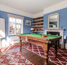 A room with a pool table in the center, bookshelves, a fireplace with a mirror, and a window with diamond-shaped panes at Church Farm Dunwich Near Westleton