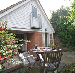 A patio area with a wooden table and chairs outside a house with a white upper wall in Mariners Cottage King Street Aldeburgh