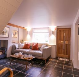 A sitting area with a sofa and cushions a coffee table with tea set a wood stove and wooden front door at Mariners Cottage King Street in Aldeburgh
