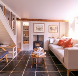 A living room with a sofa with cushions a coffee table with tea set a fireplace and a chair at Mariners Cottage King Street Aldeburgh