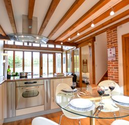 A kitchen and dining area with a glass table set for four and wooden beams on the ceiling at Two Chantry Barns Orford