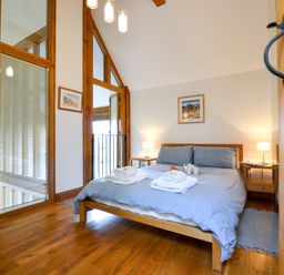 A bedroom with a wooden bed and blue bedding two bedside tables with lamps wooden floor and wall art at Two Chantry Barns Orford