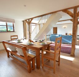 A dining area with wooden table and chairs next to a living room with blue sofas and a stove at Wheelwright's Barn in Walpole Near Halesworth