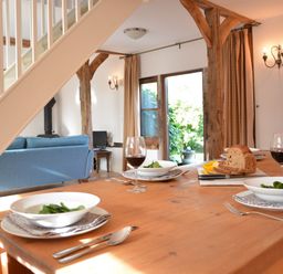 A dining table set with bowls of salad red wine glasses and sliced bread in a room with wooden beams and a blue sofa at Wheelwright's Barn Walpole Near Halesworth