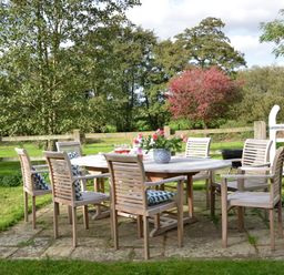 An outdoor dining area with a wooden table and chairs on a stone patio in a fenced garden at Wheelwright's Barn Walpole Near Halesworth