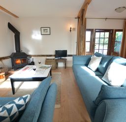 A living room with blue sofas a wood burning stove and a coffee table at Wheelwright's Barn in Walpole Near Halesworth