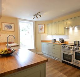 A kitchen with wooden countertops a stainless steel oven a sink with a faucet a bowl of fruit and framed pictures on the walls at Henstead Hall Henstead near Beccles