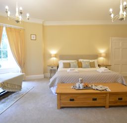 A bedroom with a bed side tables lamps window with curtains bench and a wooden coffee table with breakfast tray at Henstead Hall Henstead near Beccles