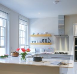 A kitchen with two large windows flowers on the counter and floating shelves holding mugs and jars at 10 Church Walk Aldeburgh