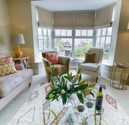 A living room with two armchairs and a sofa around a glass coffee table with flowers and wine at 10 Church Walk Aldeburgh