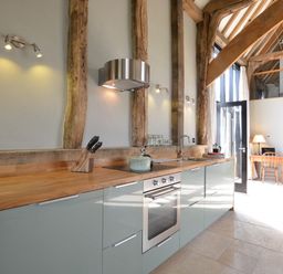 A kitchen with wooden countertops, modern cabinets, built-in oven, and visible wooden beams at Manor House Barn Peasenhall