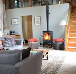 A living room with a wood burning stove and wooden staircase at Manor House Barn Peasenhall