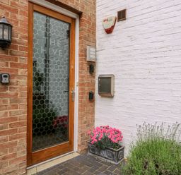 A wooden door with frosted glass and the words The Hive on it between brick and white walls with a flower box and outdoor light at The Hive Southwold