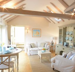 A living room with a dining table, sofa, armchair, cabinet with plates, and a coffee table at The Nookery at Snape Hall in Snape Suffolk