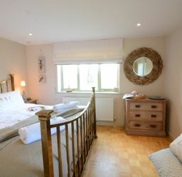 A bedroom with a brass bed, wooden chest of drawers, window with white blind, and a bench with a bunny pillow at The Nookery at Snape Hall in Snape Suffolk