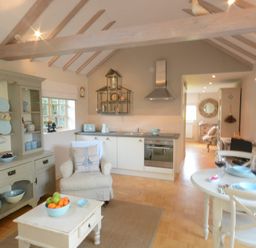 A kitchen and dining area with a cabinet, armchair, table with wine glasses, and pendant lighting at The Nookery at Snape Hall Snape Suffolk