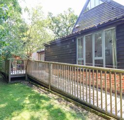 A garden view with grass a wooden deck and railing attached to a house with large windows at Yew Tree Farm Stable Worlingworth