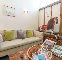 A sitting area with a beige sofa and green and gray cushions a wooden coffee table with magazines and a toy rocking horse in the corner at Yew Tree Farm Stable Worlingworth