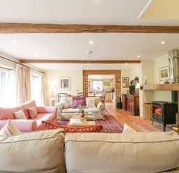 A living room with sofas a wood stove exposed beams and a kitchen visible at The Cart House Sudbourne Near Orford