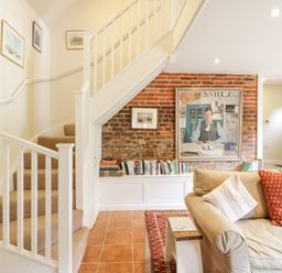 A living room with a staircase a bookshelf and a sofa with cushions at The Cart House in Sudbourne Near Orford