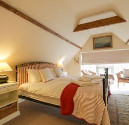 A bedroom with a double bed bedside tables lamps two wicker chairs and a window with blinds at The Cart House in Sudbourne Near Orford