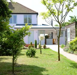 A garden with trees and bushes leading to a house with glass doors and a wooden shed on the right at 2 Pink Cottages Aldeburgh