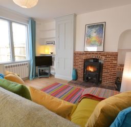 A living room with a fireplace television colorful cushions and a striped rug at 2 Pink Cottages Aldeburgh