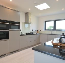 A modern kitchen with built-in ovens a stovetop under a glass hood a sink below a window and a countertop with a tray holding a teapot and cups at Skylight Aldeburgh in Aldeburgh