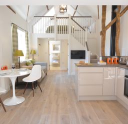 A kitchen and dining area with white table and chairs a sofa and staircase leading to a loft bedroom at Carriage House Bruisyard Near Framlingham