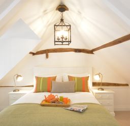 A bedroom with a double bed two bedside tables with lamps and exposed wooden beams at Carriage House Bruisyard Near Framlingham