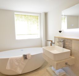 A bathroom with a standalone bathtub towel and book a rectangular sink under a lit mirror at Carriage House Bruisyard Near Framlingham