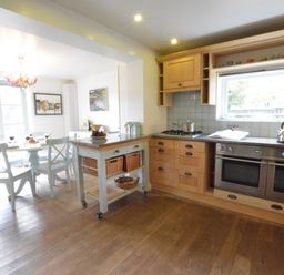 A kitchen with wooden cabinets a dining table with chairs and a mobile island unit at Robert Sadler's Studio in Aldeburgh