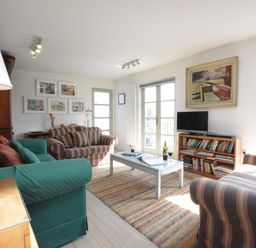 A living room with striped and green sofas a coffee table with wine glasses a TV on a bookshelf and wall art at Robert Sadler's Studio in Aldeburgh