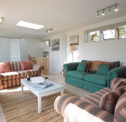 A living room with two striped sofas and one green sofa a white coffee table and paintings on the wall at Robert Sadler's Studio in Aldeburgh