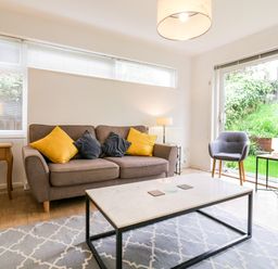 A living room with a sofa holding yellow and gray cushions a coffee table two armchairs and lamps at The Bridge House in Southwold