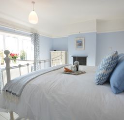 A bedroom with a white bed blue and white pillows blue patterned curtains and a tray with breakfast on the bed at Somewhere Only We Know in Aldeburgh